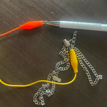 Connecting a metal chain to an alligator clip and testing it as a touch-based input, draping and holding the chain to explore how its flexibility changes the interaction.